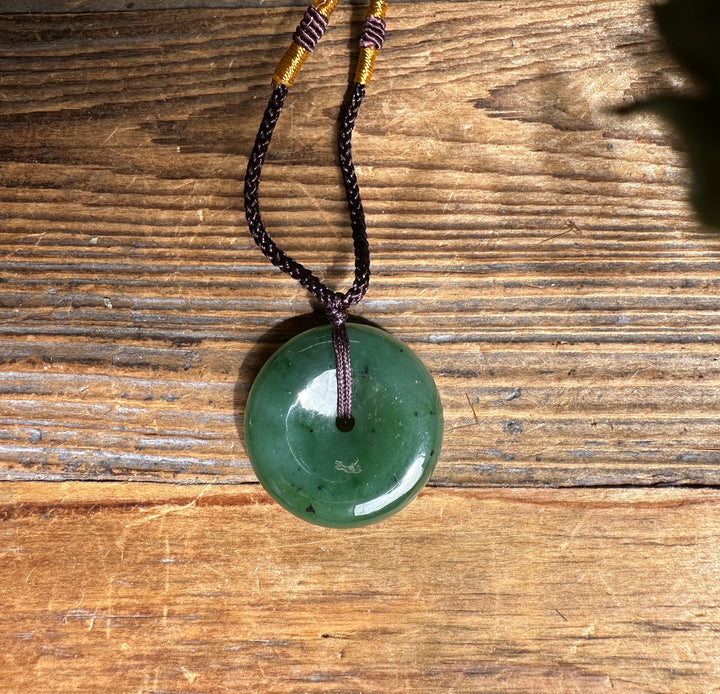 Green jade donut pendant threaded on a double brown braided cord with yellow wrapped accents.
