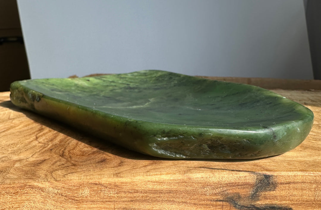 A green polished stone tray with a natural organic shape, resting on a wooden tabletop against a neutral gray background.