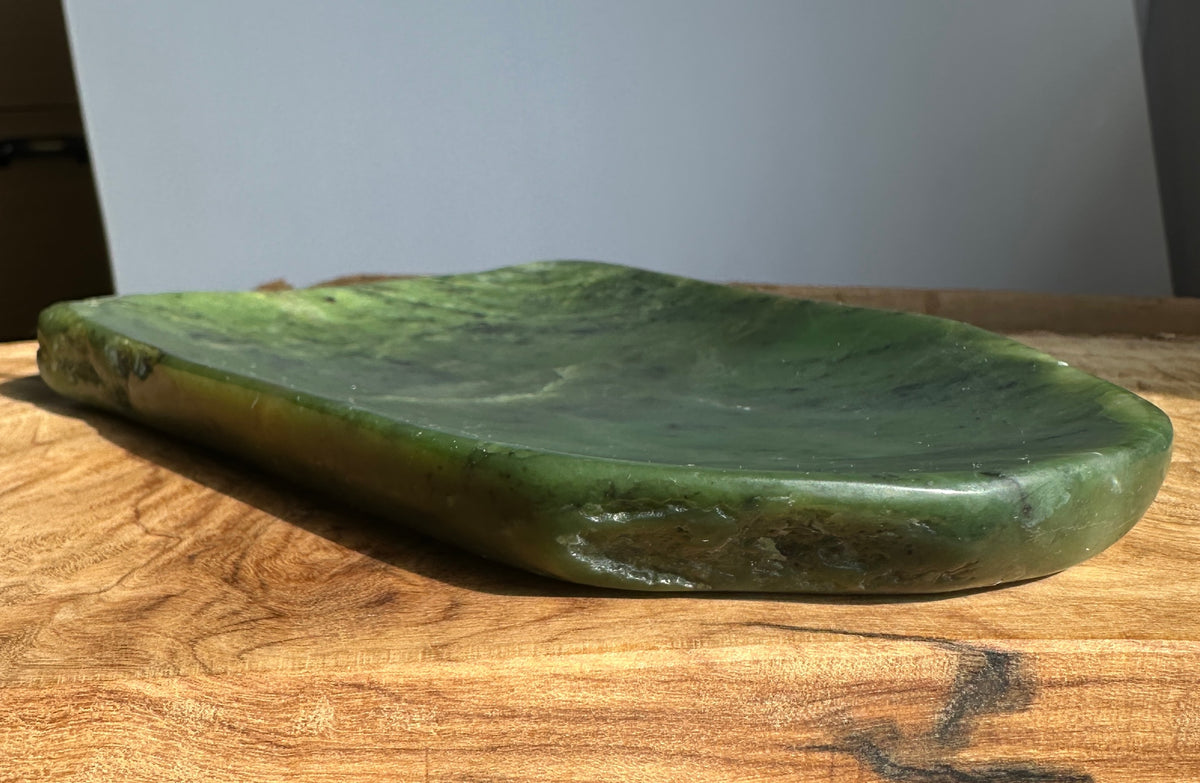 A green polished stone tray with a natural organic shape, resting on a wooden tabletop against a neutral gray background.