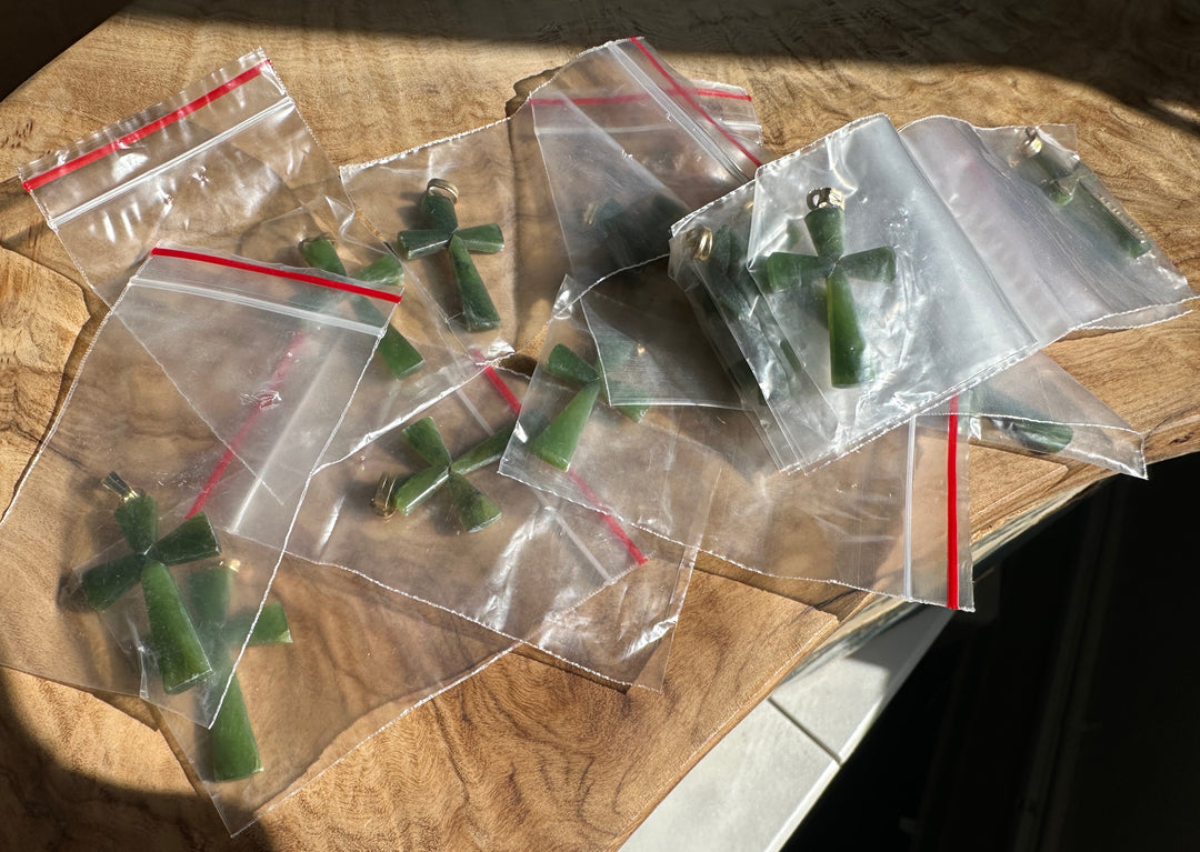 Several clear plastic zip-top bags containing green cross-shaped jewelry pieces, photographed on a wooden surface in natural sunlight.