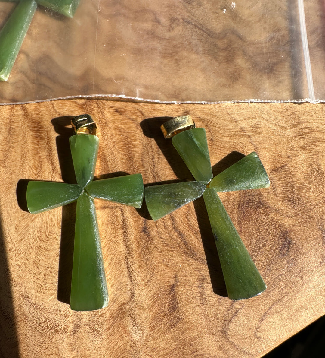 Two green cross pendants made of carved stone, displayed on a wooden surface next to a clear plastic bag.