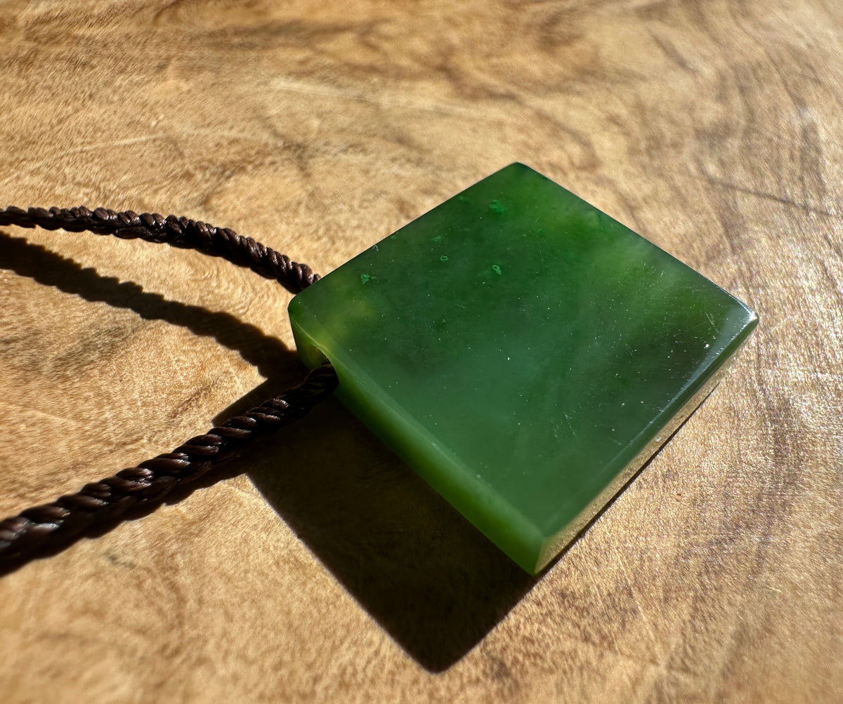 Canadian Jade Square Pendant with brown braided cord and green beads on wood.