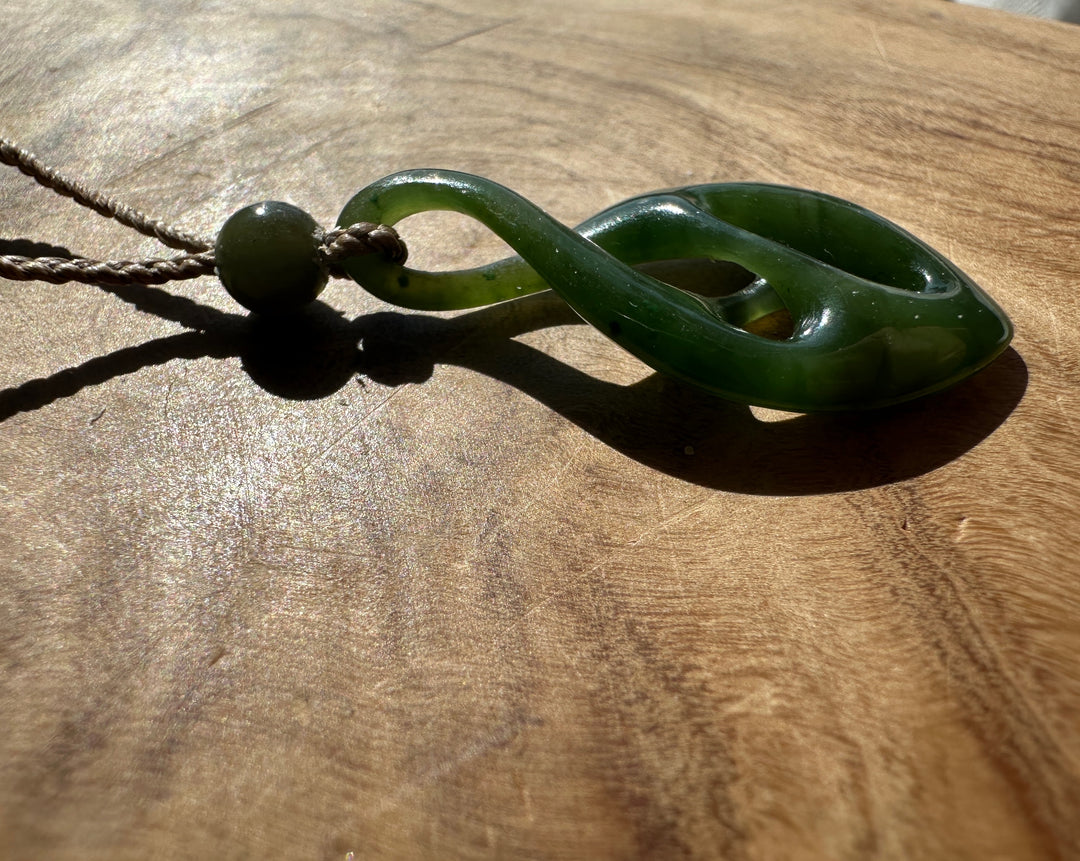 Side view of a green jade twist pendant on a wooden surface