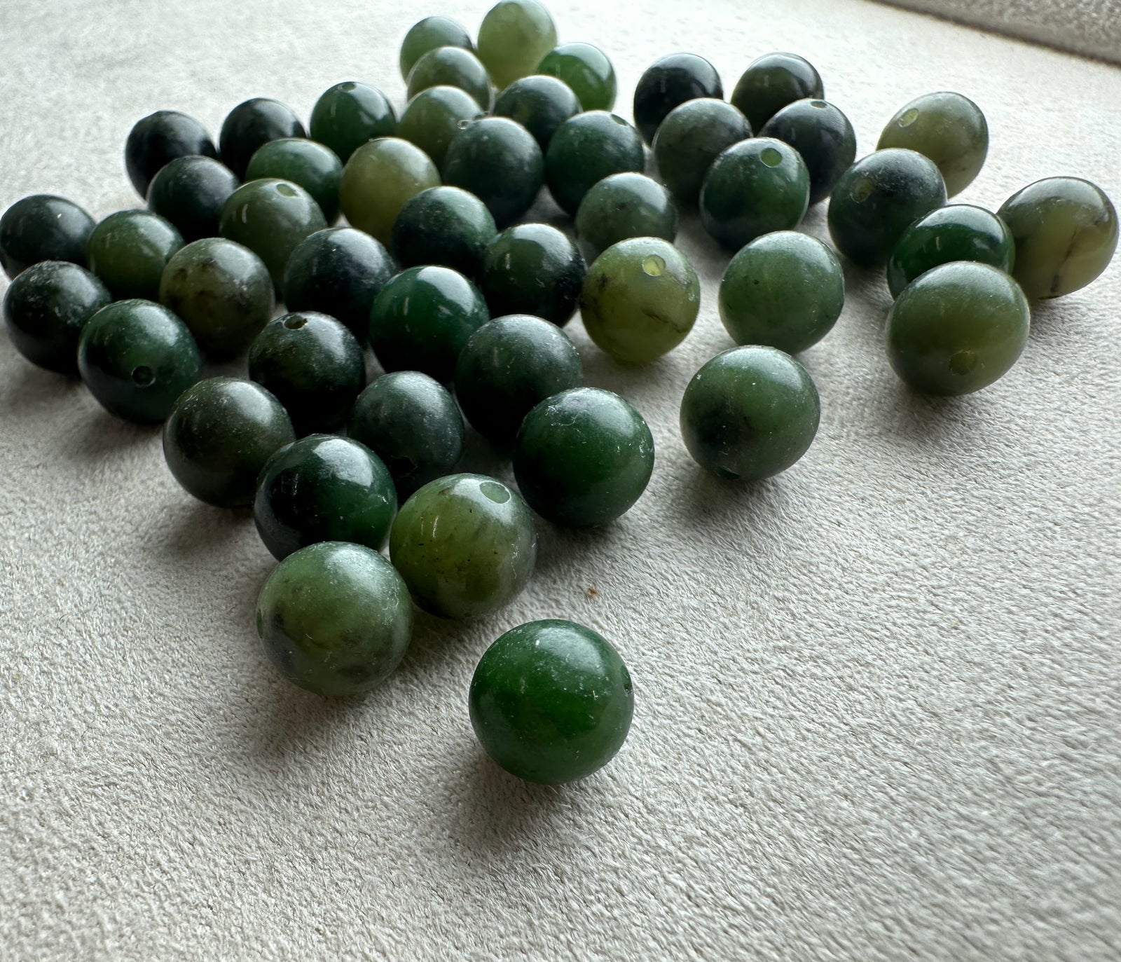 Assorted natural Canadian nephrite jade beads 7-8.5mm mix in greens scattered on a neutral surface
