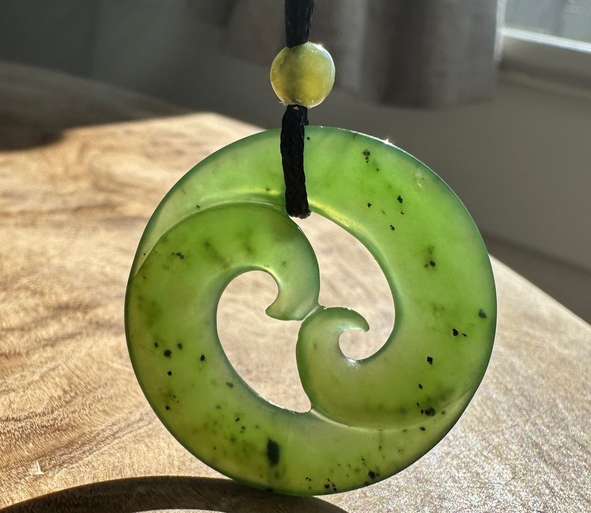 Green jade pendant beside a bright window, on a wooden base