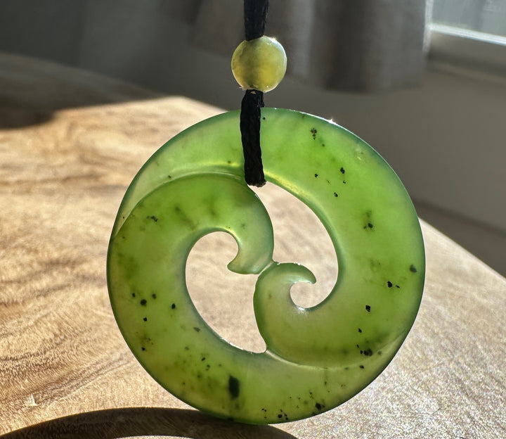 Green jade pendant beside a bright window, on a wooden base