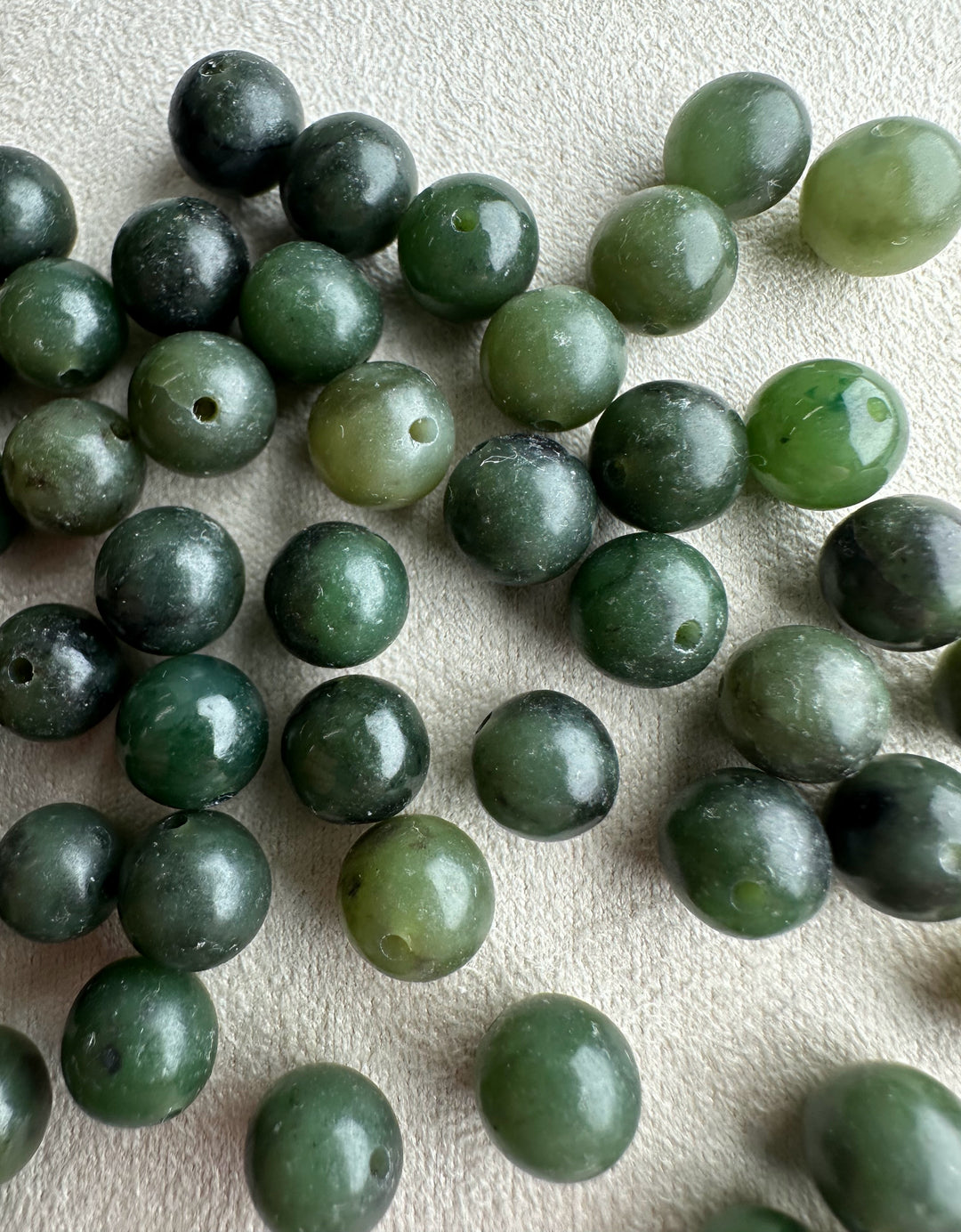 Close up of nephrite jade beads 7-8.5mm with drilled holes in dark to light green hues