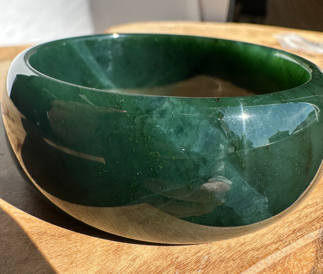 A polished dark green jade bangle bracelet resting on a wooden surface.