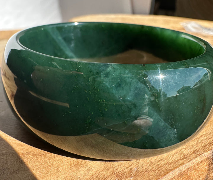A polished dark green jade bangle bracelet resting on a wooden surface.