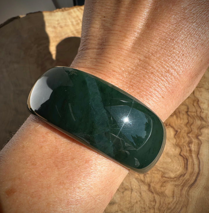 A polished dark green jade bangle bracelet worn on a person&