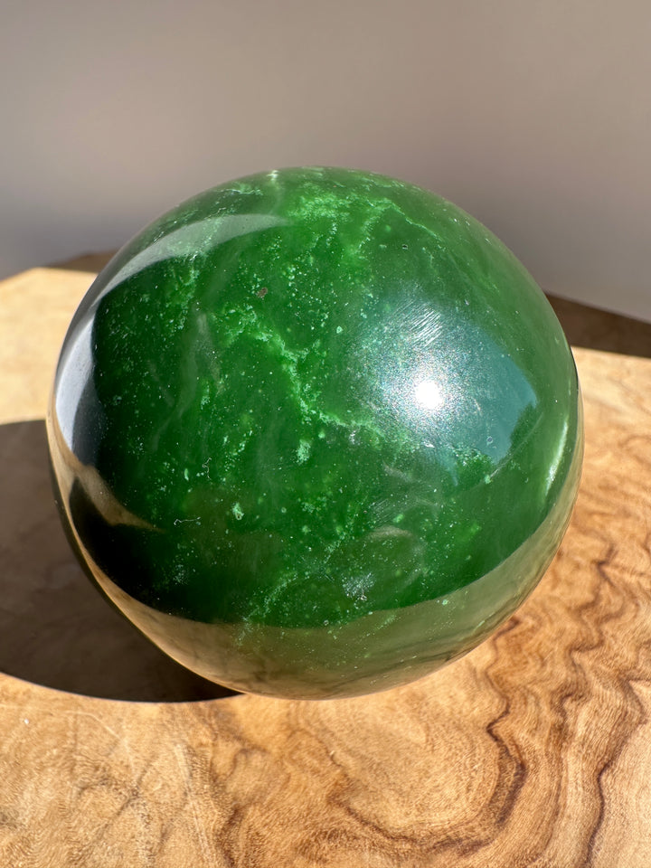 Canadian Jade Sphere 66mm resting in a metal display on a wooden surface, glossy green with light reflections.