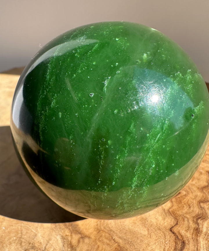 Side view of a 66mm Canadian Jade Sphere showing vivid green tones and white veins on wood.