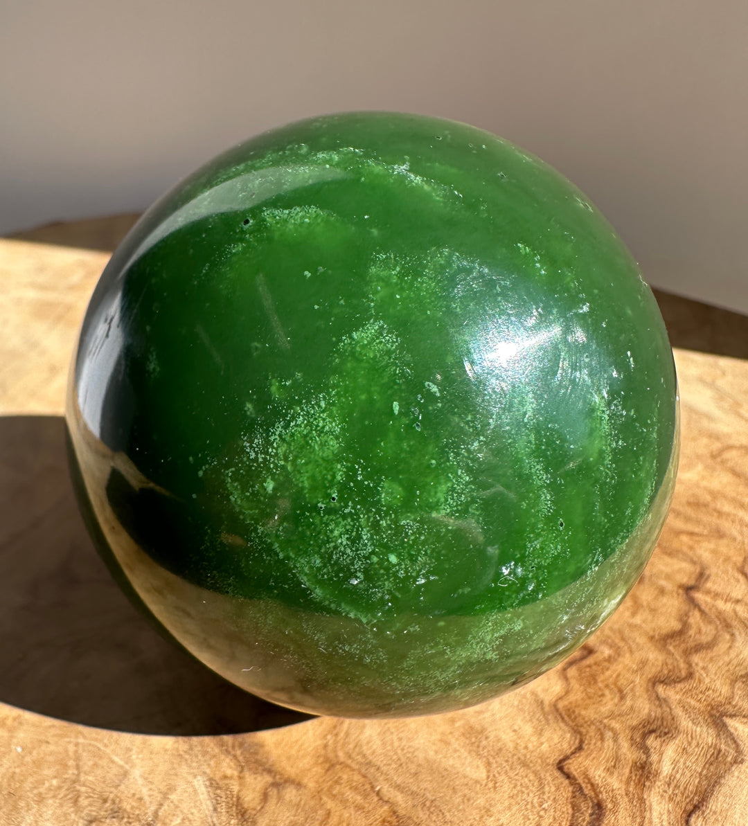 Canadian Jade Sphere 66mm close up showing vivid green jade and surface texture on a wooden surface.