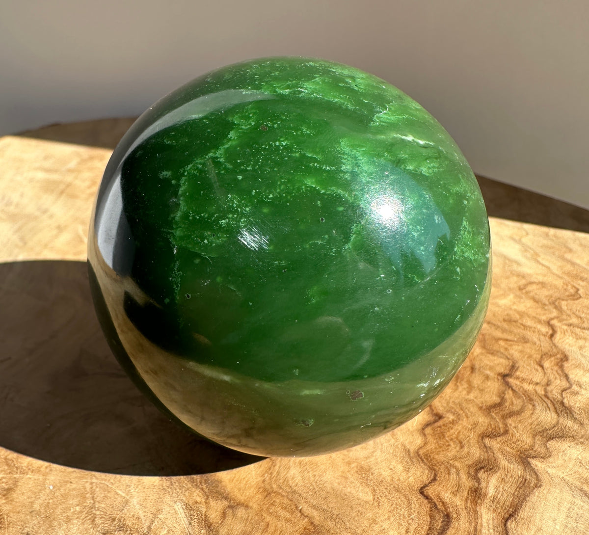 Top portion of a 66mm Canadian Jade Sphere with bright green hues and natural veining on a neutral background.