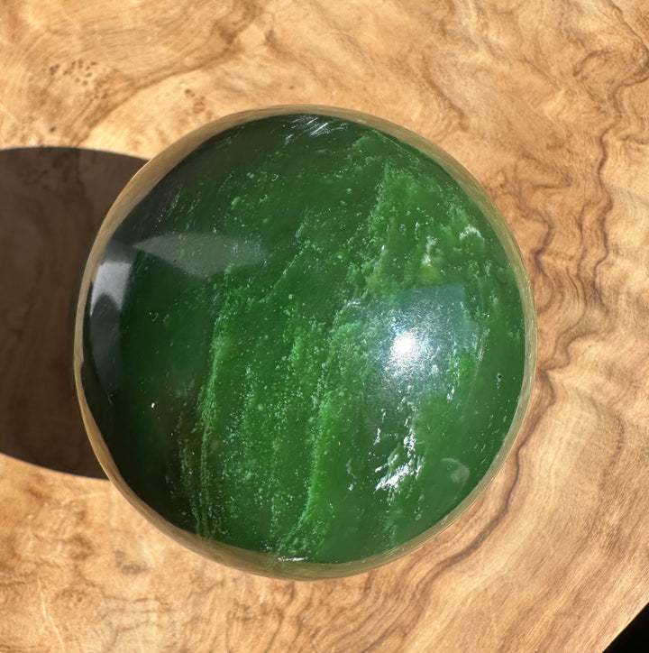 Canadian Jade Sphere 66mm polished green jade ball on a wooden surface with subtle reflections.