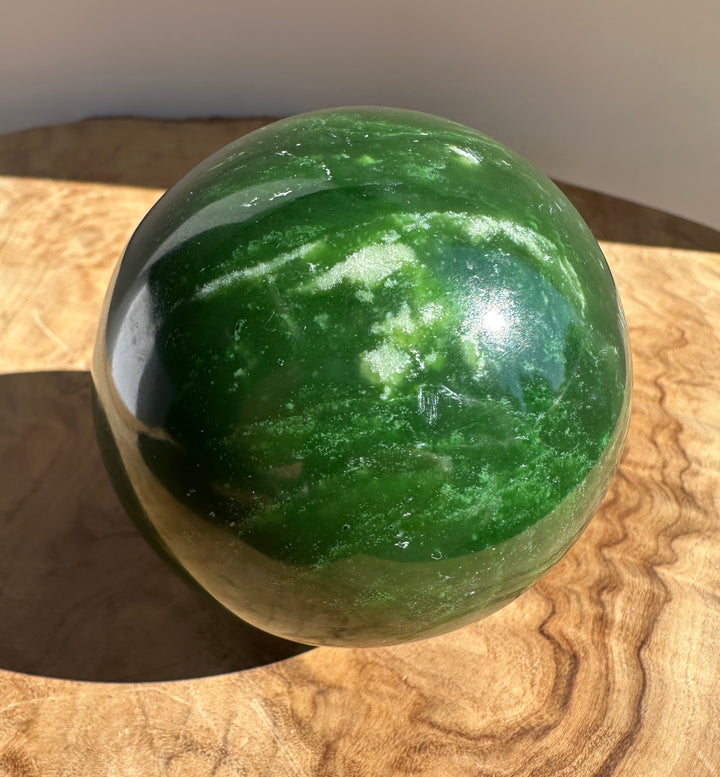 Polished Canadian jade sphere 66mm on a wooden surface.