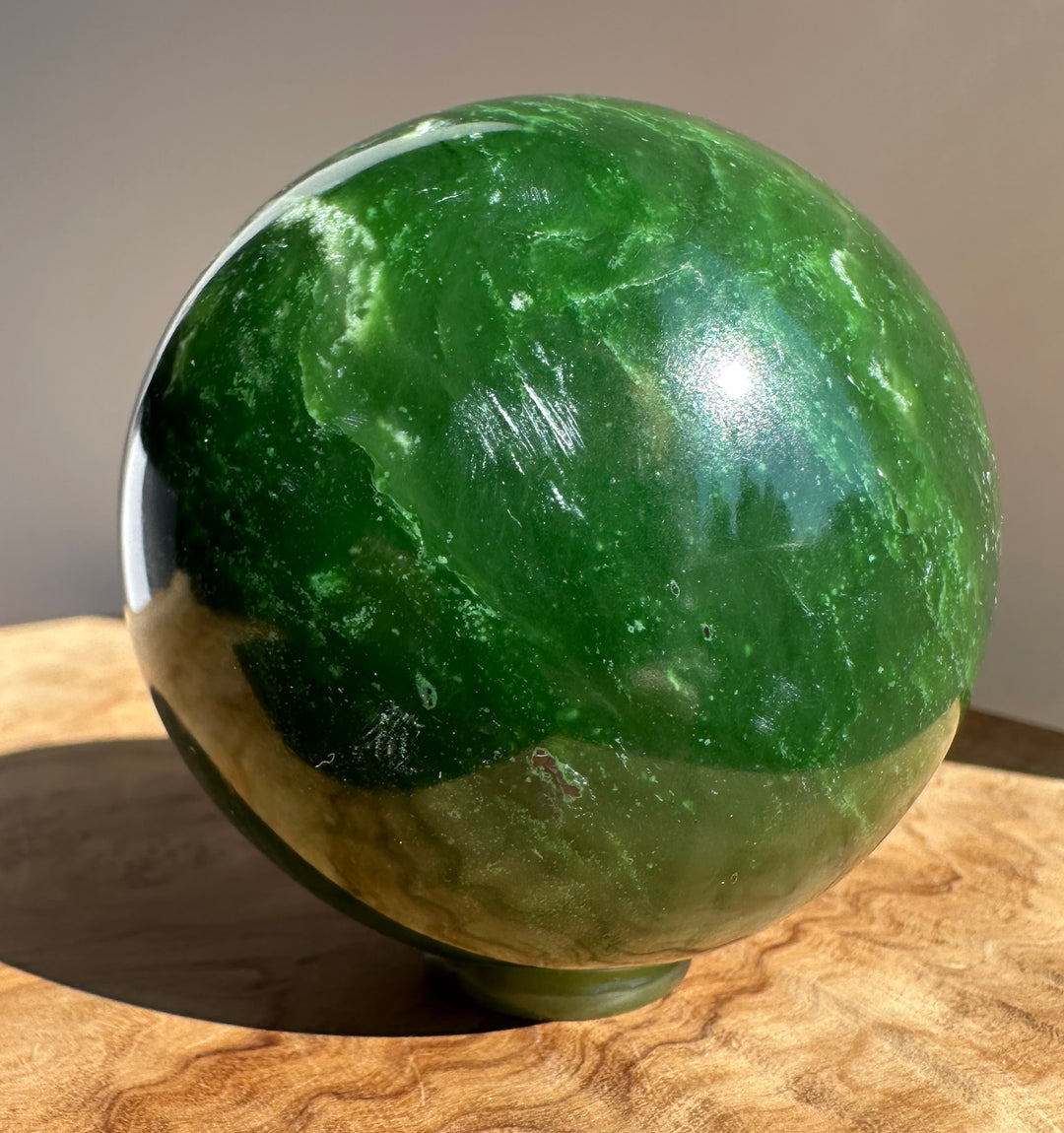 Close-up of a 66mm Canadian Jade Sphere with deep green marbling resting on a wooden surface.