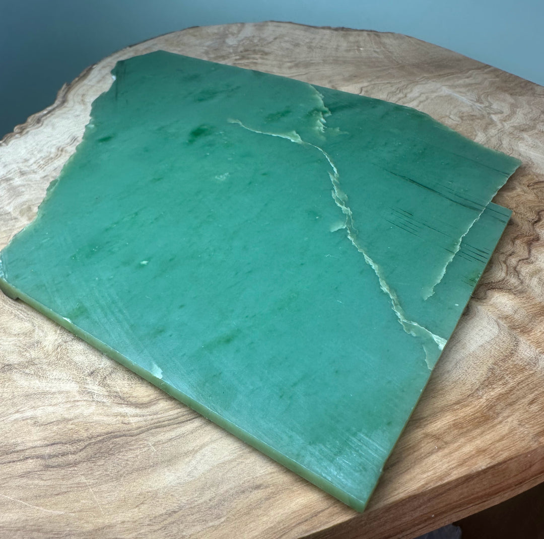 A+ Siberian nephrite jade slab in teal green on a wooden surface with a pronounced diagonal crack