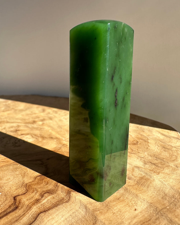 A polished green jadei rectangular block standing upright on a wooden surface against a neutral beige background.