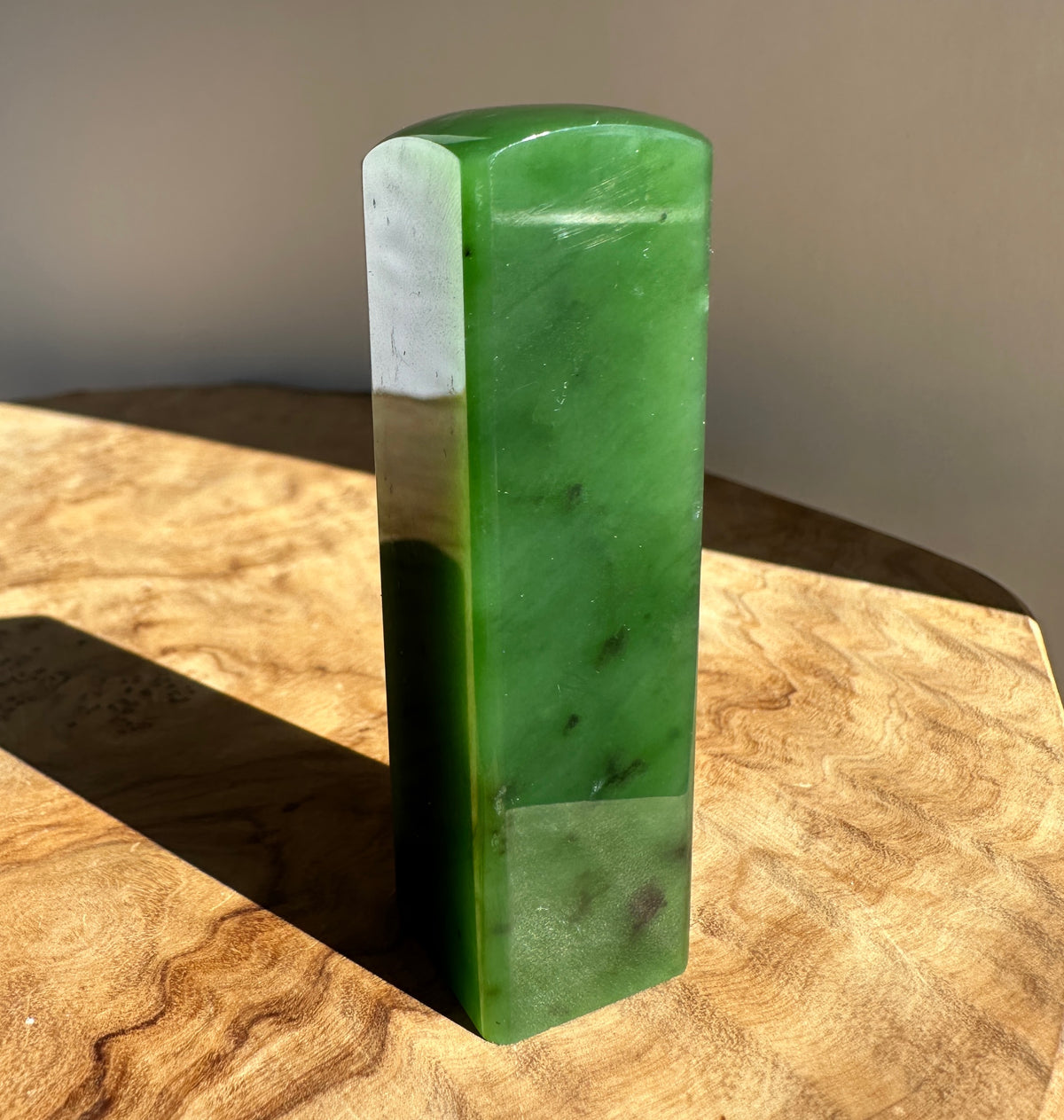 A polished green jade rectangular block with rounded top corners, standing upright on a wooden surface in warm natural light.