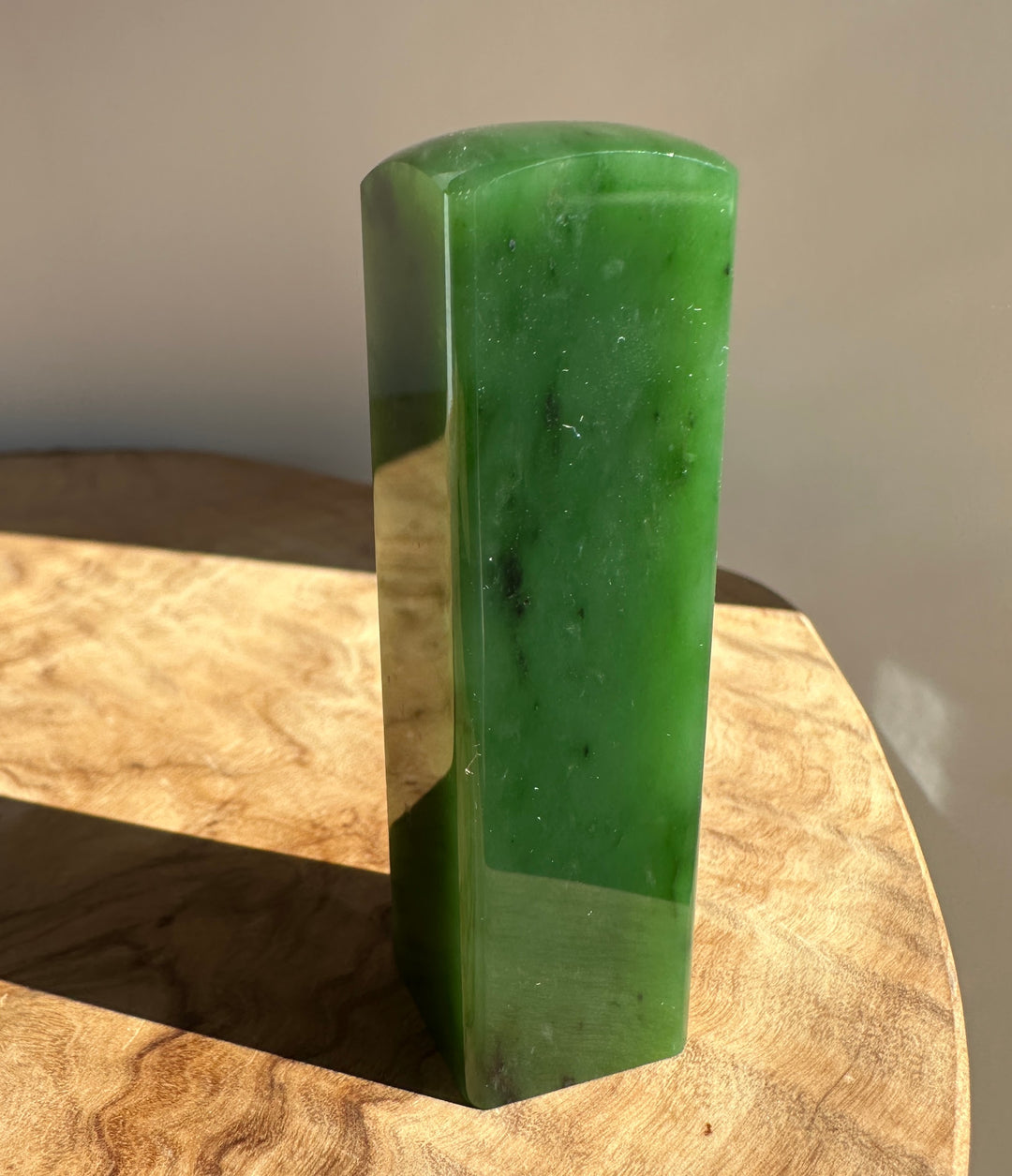 A polished green jadei rectangular block with rounded top corners, standing upright on a wooden surface against a neutral background.