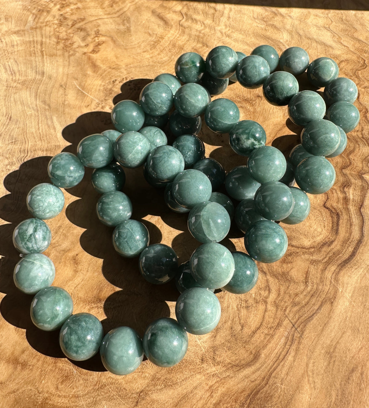 A beaded bracelet made of polished round green stone beads, arranged in a loose circle on a wooden surface.