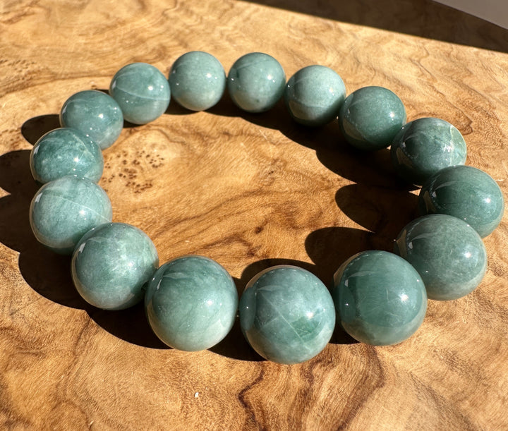 A beaded bracelet made of polished round teal-green gemstone beads, arranged in a circle on a textured wooden surface.