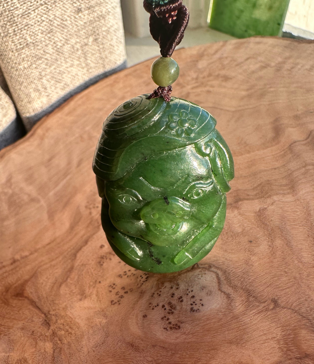 Close up of a hand carved green jade pig pendant on a braided cord with a green bead