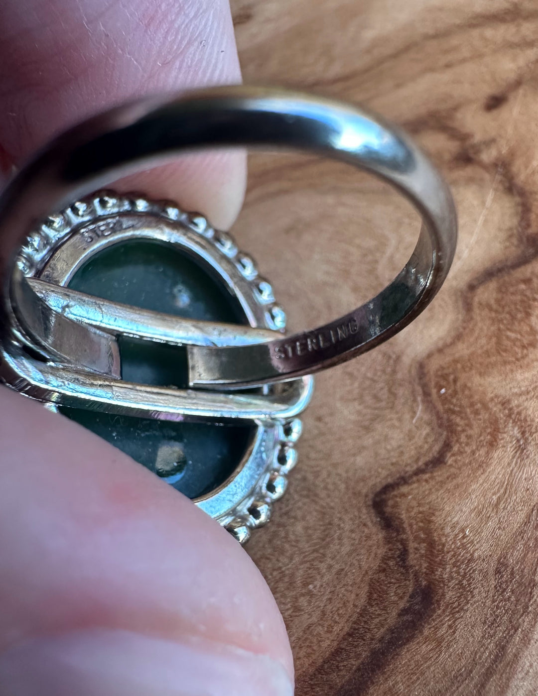 Close up of vintage green jade ring with silver setting and beaded edge, stamped sterling