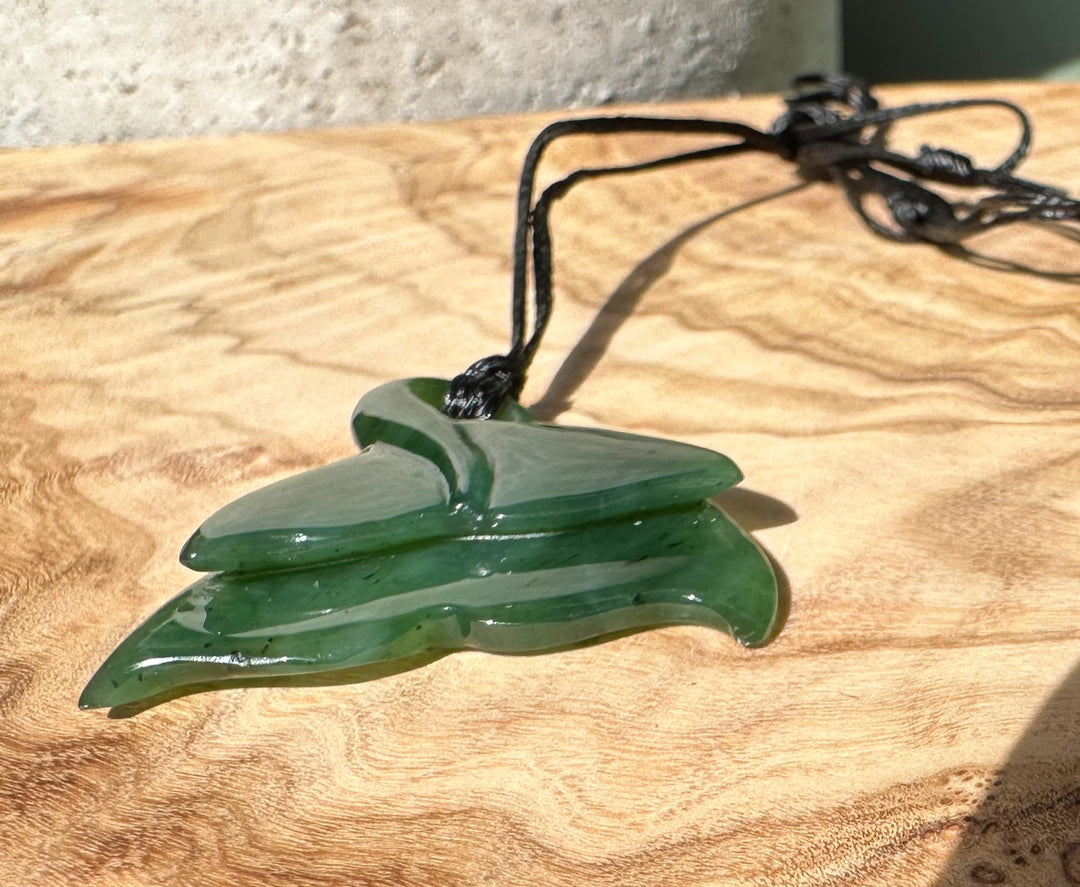 Green jade whale tail pendant on black cord resting on a wooden surface