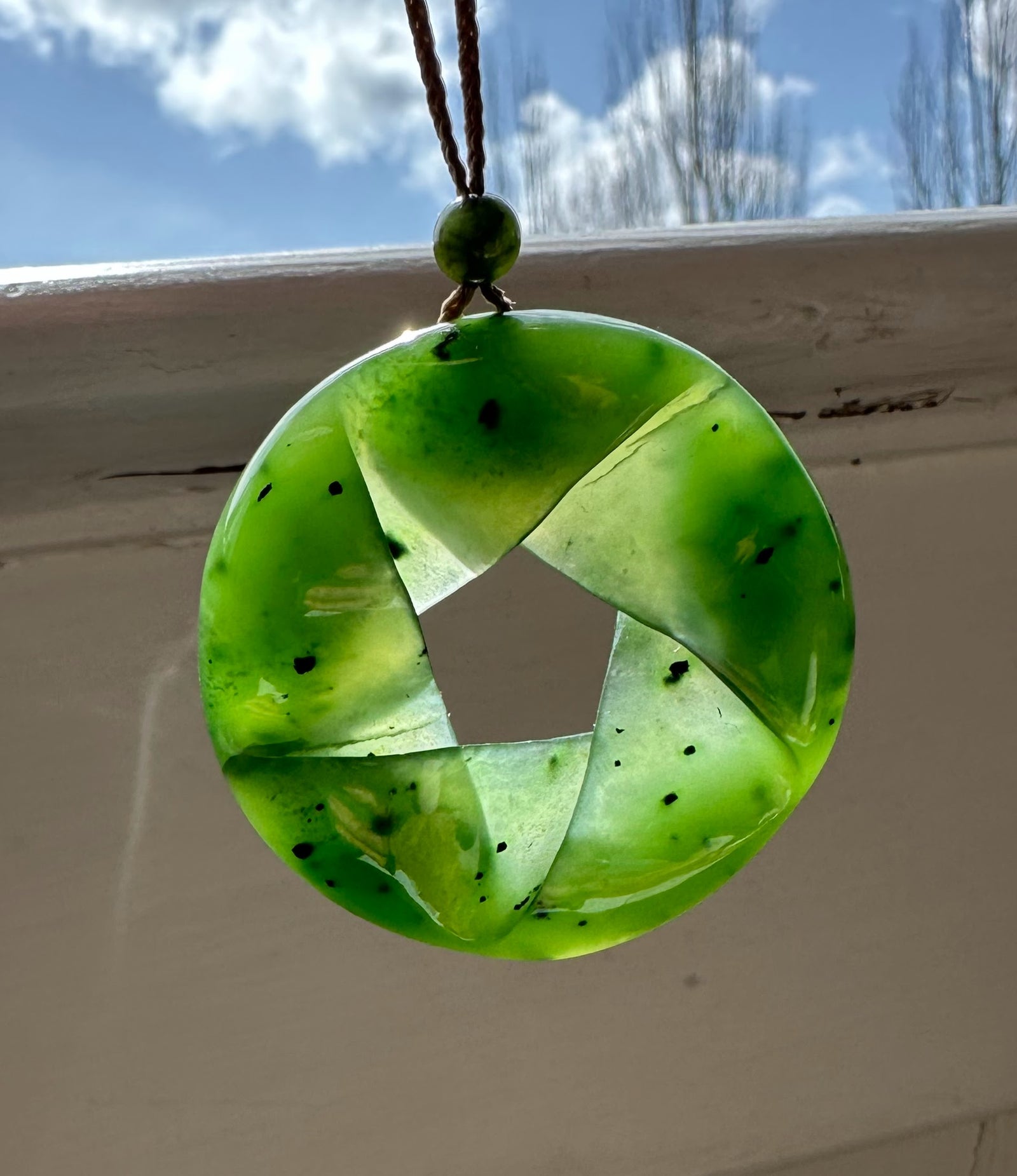 Green fractured AA nephrite jade pendant shaped as a circular wheel with four twisted segments speckled with black flecks.