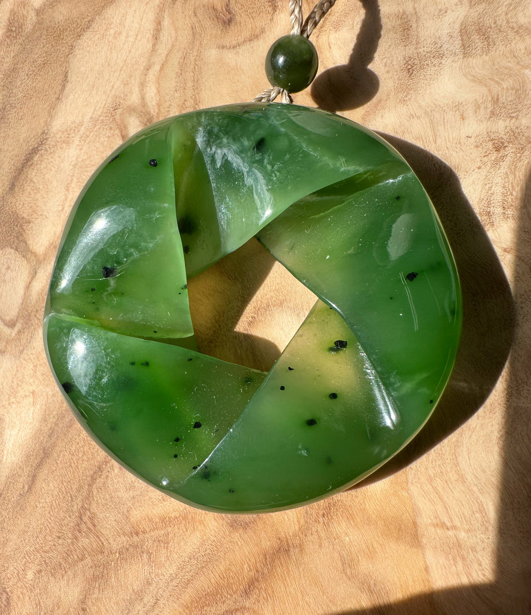 Green nephrite jade circular pendant with four curved segments forming a hollow center on a beige rope with a green bead.