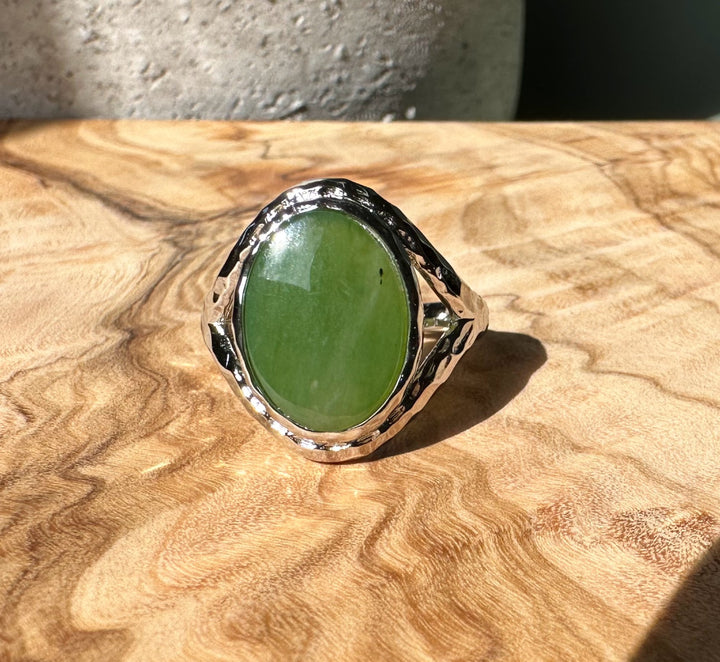Canadian Jade and Silver Ring with an oval green jade cabochon set in a hammered silver band on a wooden surface.