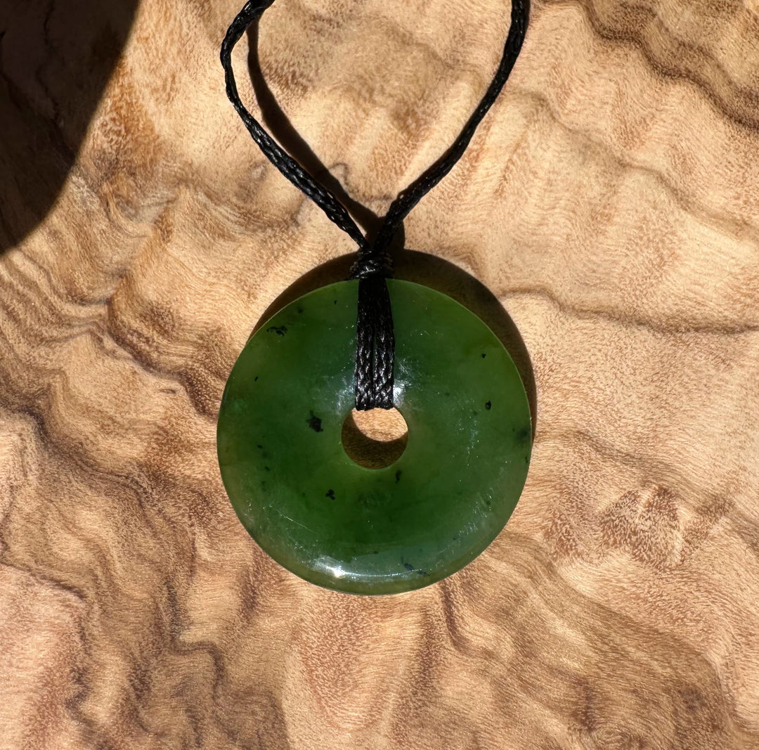 Green jade donut pendant with a central hole suspended from a black cord