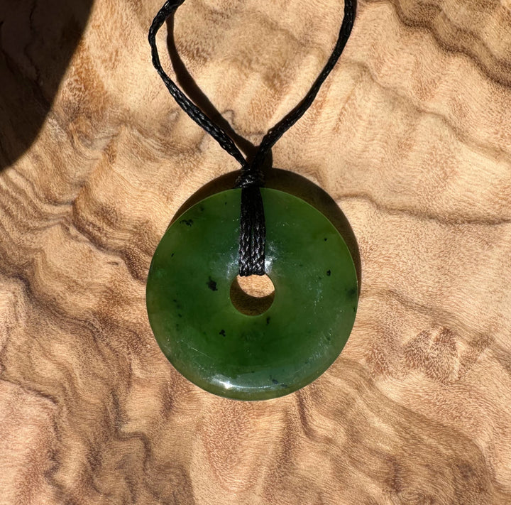 Green jade donut pendant with a central hole suspended from a black cord