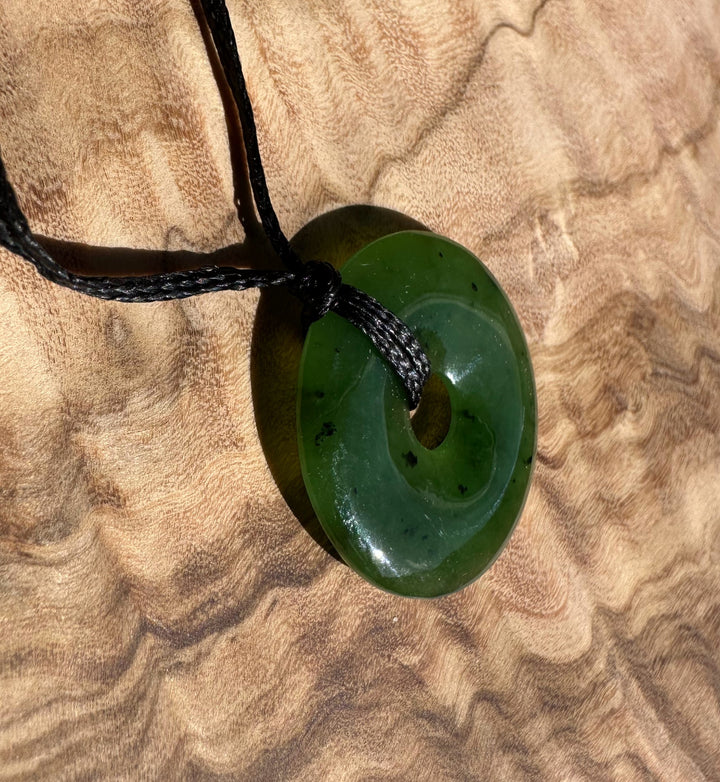 Dark green jade 25mm donut pendant on a black cord against a textured beige background.