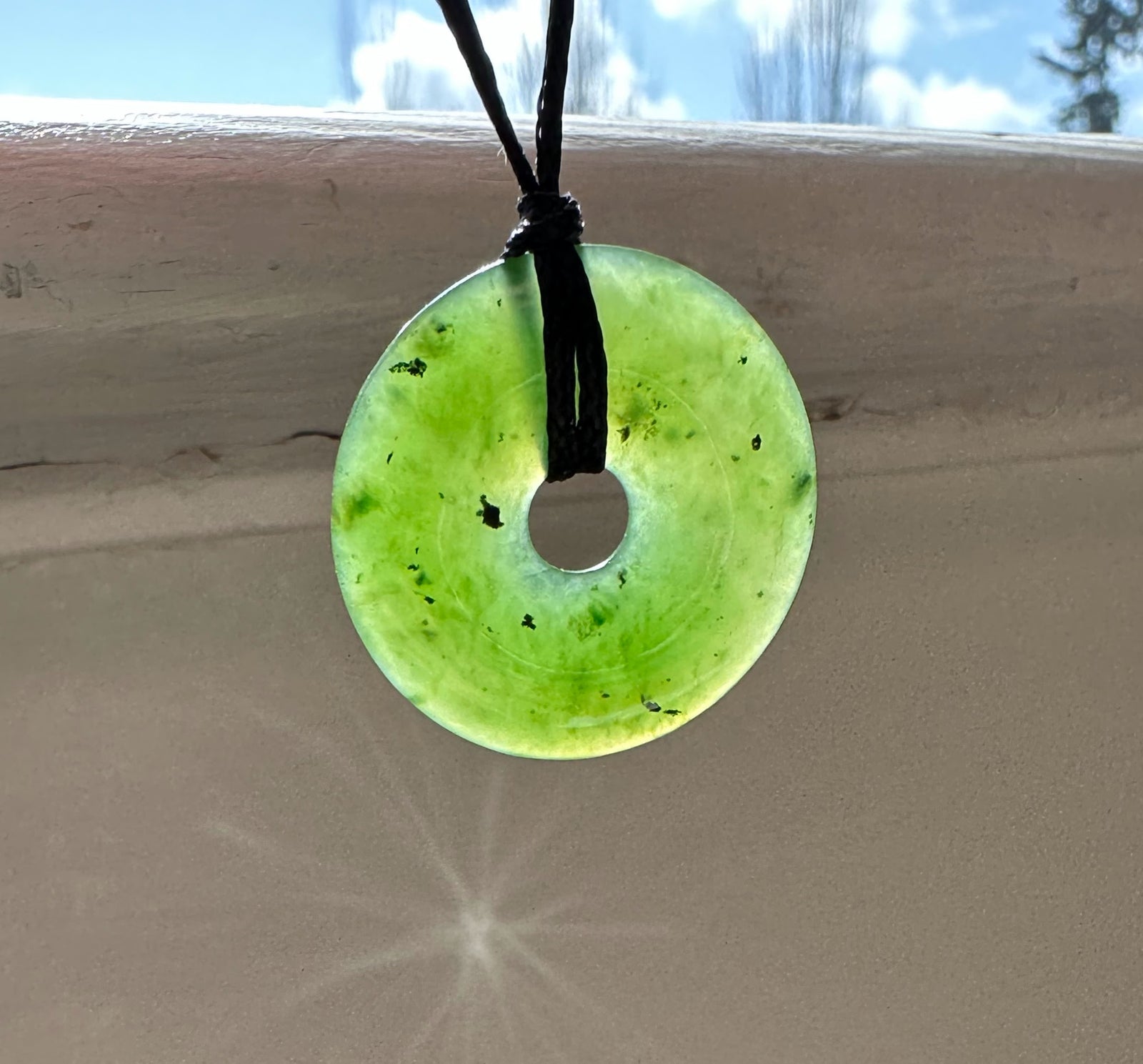 Light green jade 25mm donut pendant on a black cord against a blue sky.