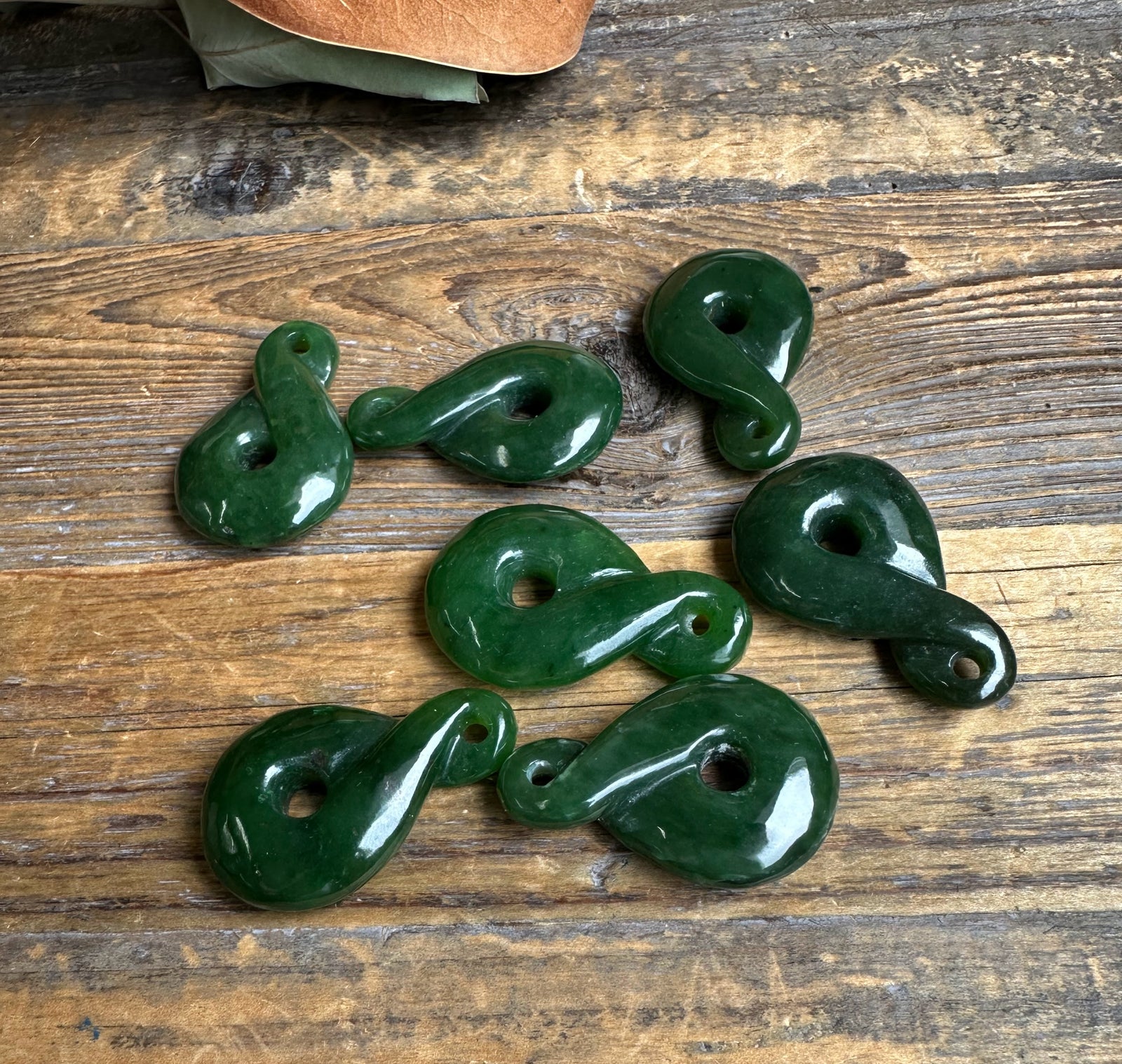 Dark green jade infinity twist pendants with holes arranged on a rustic wooden surface