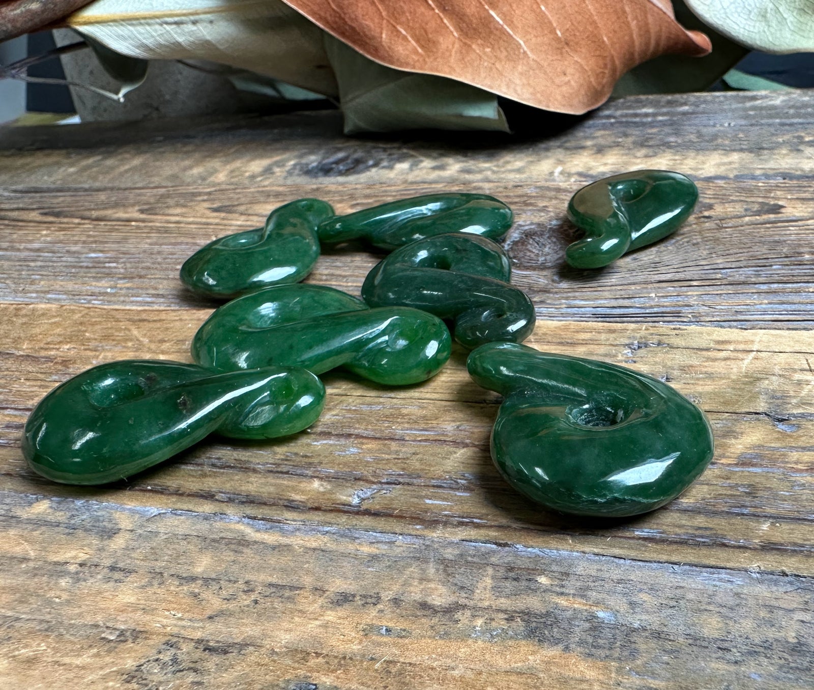 Dark green jade infinity twist stones scattered on a rustic wooden tabletop with dried leaves overhead