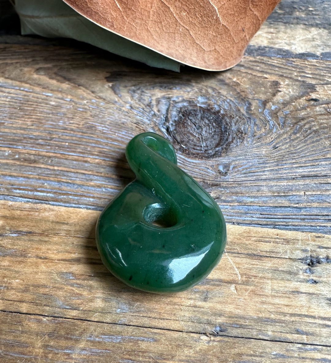 Close up of dark green jade infinity twist pendant resting on a textured wooden surface