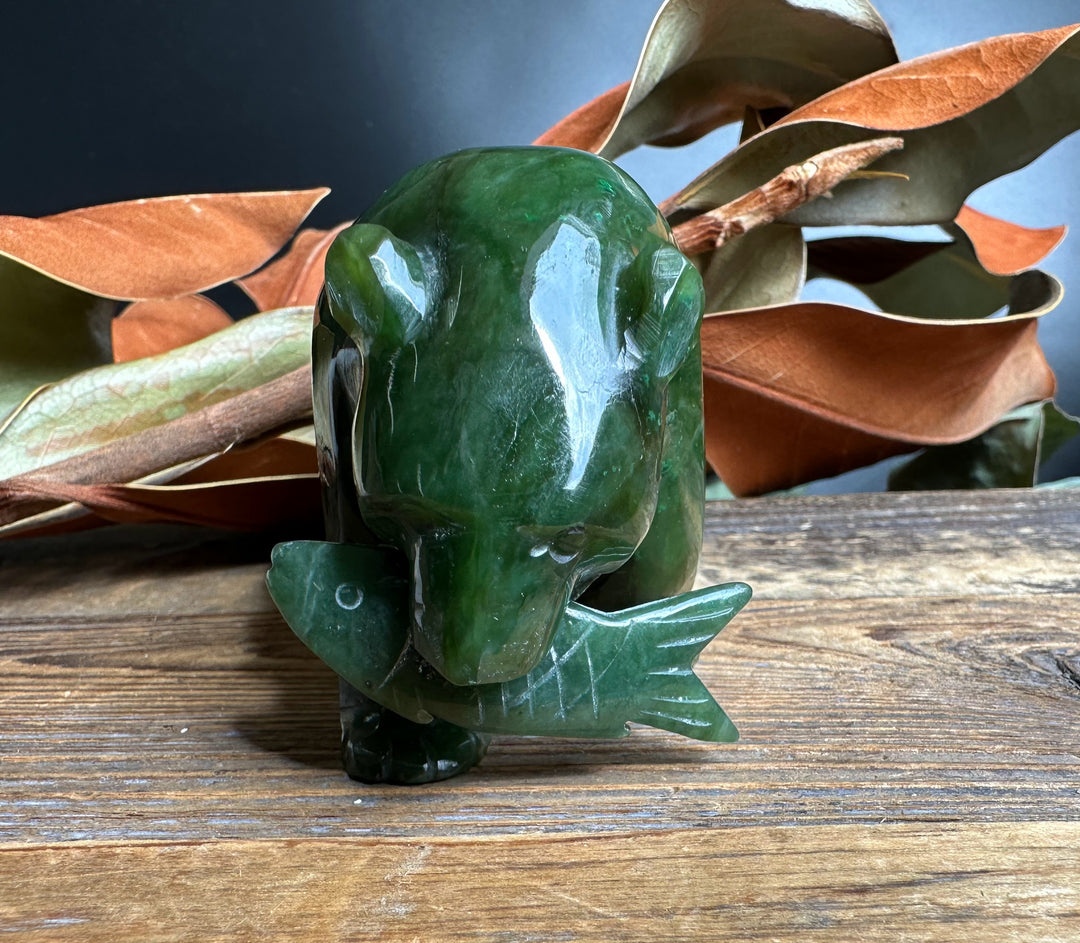 Green jade bear sculpture with a carved jade fish in its mouth on a wooden surface
