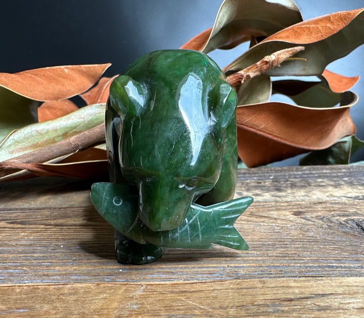 Green jade bear sculpture with a carved jade fish in its mouth on a wooden surface