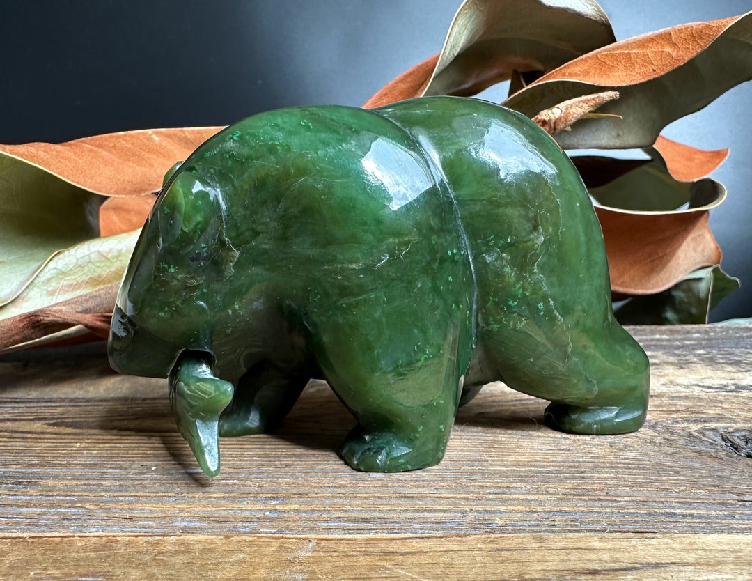 Green jade bear statue with a jade fish in its mouth on a rustic wooden surface