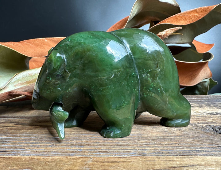 Green jade bear statue with a jade fish in its mouth on a rustic wooden surface