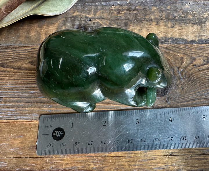 Top view of a green jade bear sculpture on a wood surface with an inch ruler for scale