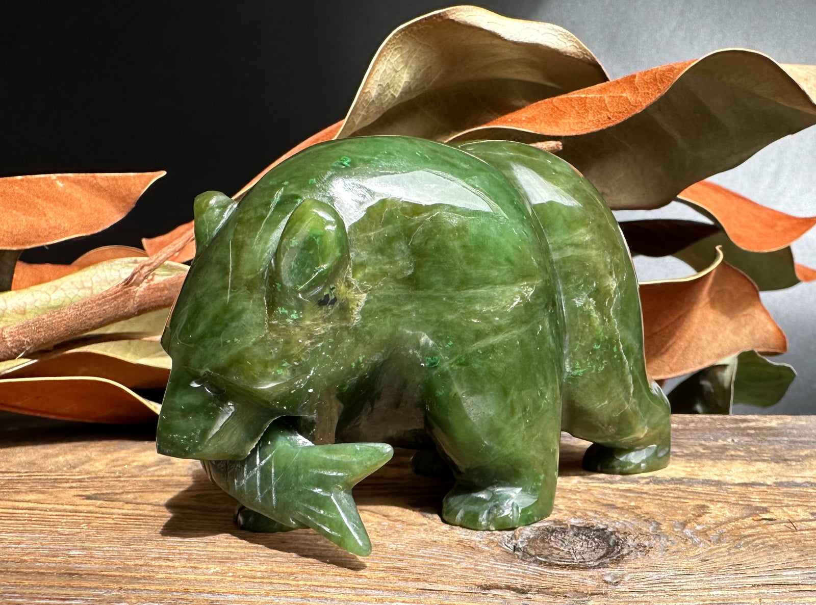 Side view of a green jade bear with a jade fish in its mouth.