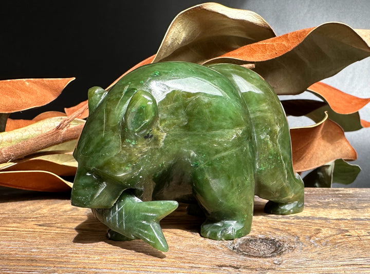Side view of a green jade bear with a jade fish in its mouth.