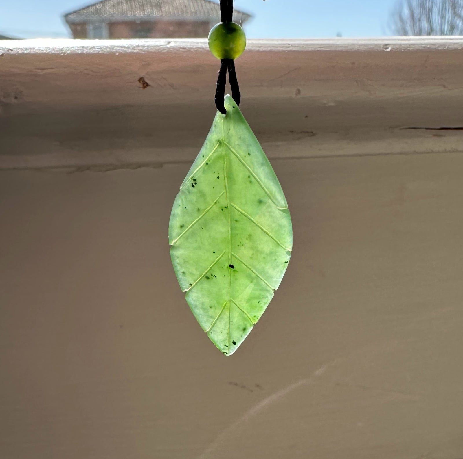 Canadian jade leaf pendant 38mm hanging from a black cord with a small green bead above