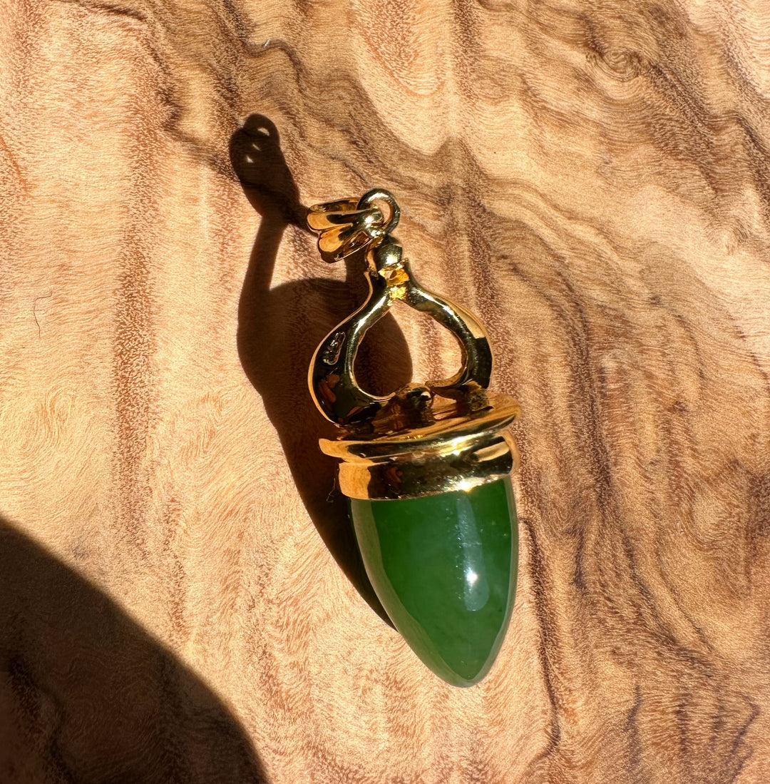 AA Canadian Pendant 0212 gold pendant with green teardrop gemstone and ornate top on warm wood surface