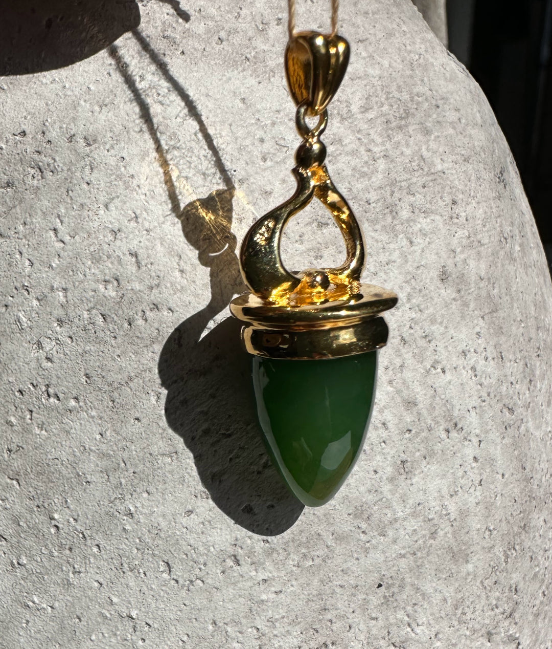 AA Canadian Pendant 0212 gold pendant with green teardrop gemstone on light stone background